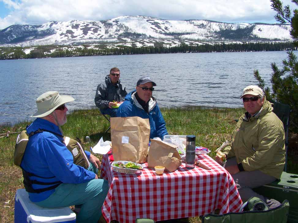 4 Fishermand sitting on shore eating a picnic lunch next to a lake